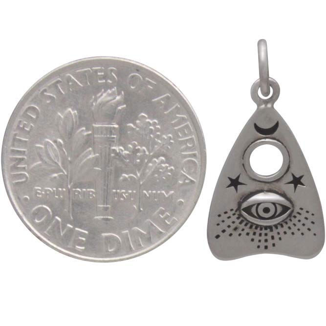 The Silver Ouija Planchette Charm with All Seeing Eye by Nina Designs captures the essence of seance planchettes with its intricate engravings of an eye, crescent moons, stars, and a dot pattern. To demonstrate its size, it is displayed next to a U.S. dime.