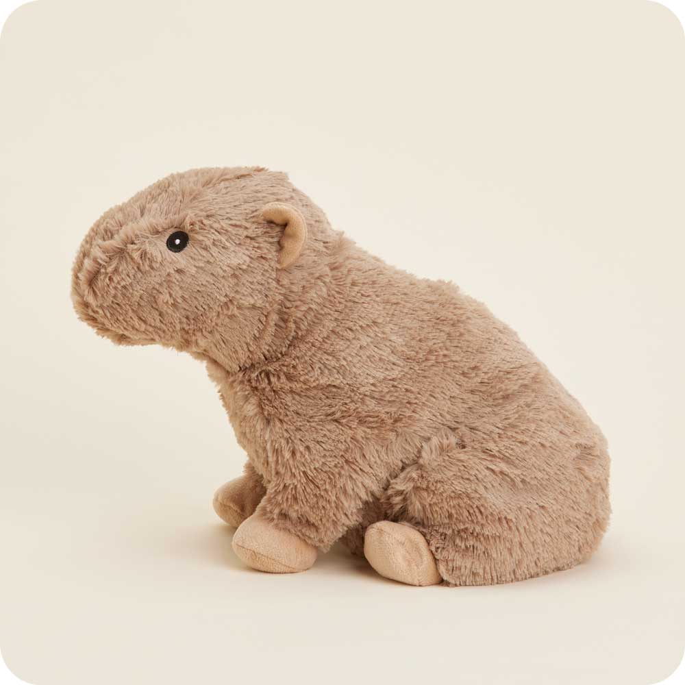 A fluffy, light-brown Capybara Warmie from Warmies sits upright against a plain, light background. This plush toy features small, round ears and dark eyes, with detailed stitching that defines its charming characteristics.