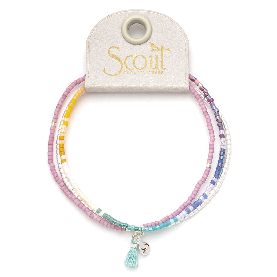 Introducing the Bright Multi Silver Miyuki Bracelet Trio from Scout Jewelry, a stunning set of vibrant stacking bracelets. These bracelets showcase a vivid array of purple, pink, yellow, and blue Miyuki Delica beads and are each adorned with a small silver charm and a turquoise tassel. They are elegantly presented on a branded card holder.