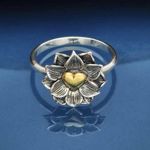 Introducing the s5 Lotus Ring with Heart by Nina Designs: a stunning silver ring featuring an intricate lotus flower motif. Delicate petals elegantly encircle a gold heart at its core, all beautifully enhanced by a dark blue gradient backdrop.