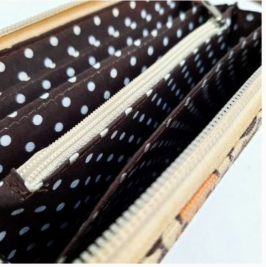 A close-up of the Zipper Wallet Happy Dog by Bungalow 360, crafted from cotton canvas, highlighting its multiple zippered compartments lined with brown fabric and white polka dots. The beige exterior showcases a subtle pattern, ideal for those who support animal causes.