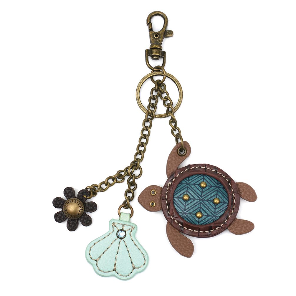 The Turtle Keychain by Chala showcases a brass lobster clasp and ring, adorned with a faux leather turtle charm featuring a blue and brown shell. It also includes a light blue shell-shaped charm and small black and gold flower charms, all elegantly connected by brass chains.