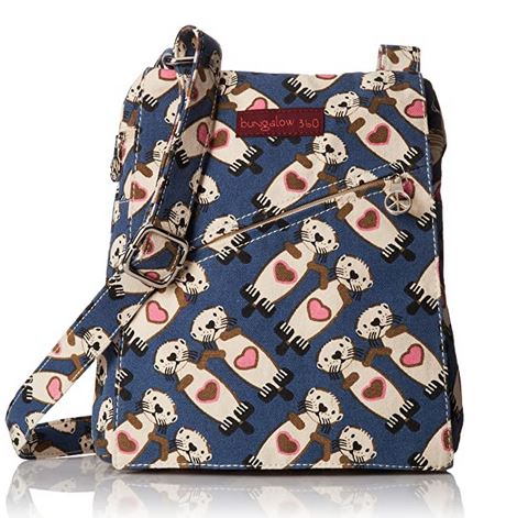 A crossbody bag with a blue background and an adorable pattern of white cartoon sea otters holding pink hearts. Made from 100% cotton, the bag features a front zippered pocket and an adjustable shoulder strap. A red tag on the front displays the brand "Bungalow 360," known for its unique designs supporting animal causes.