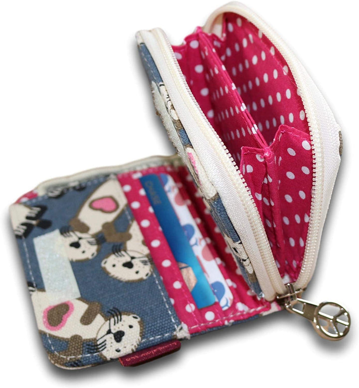 The Bungalow 360 Bill Fold Wallet Sea Otter, a small zippered wallet crafted from cotton canvas, showcases an adorable sea otter design on the exterior and a playful pattern of white polka dots on a pink background inside. Upon opening the wallet, you'll find two main compartments and a card holder displaying a blue and white card. The zipper pull is adorned with a silver heart charm.