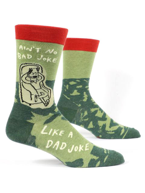 Introducing the Dad Joke Socks by Blue Q: A pair of green men's socks featuring camouflage patterns, red cuffs, and amusing illustrations. One sock portrays a reclining figure alongside the text "Ain't No Bad Joke," while the other sock displays "Like a Dad Joke" in playful fonts. Crafted from 62% combed cotton for ultimate comfort and style.