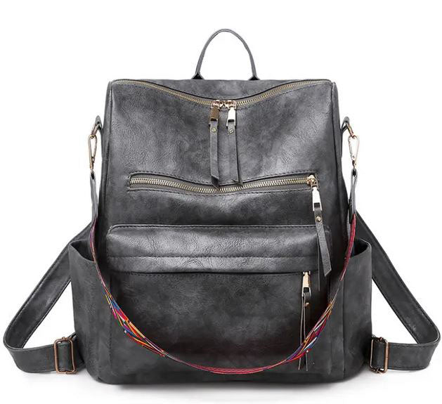 Introducing the Hailey Backpack - Grey by zzzLivFoxy: A chic grey vegan leather backpack with gold zippers and a vibrant rainbow-patterned strap. It boasts multi-functional pockets and a convenient top handle, blending practicality with modern style.