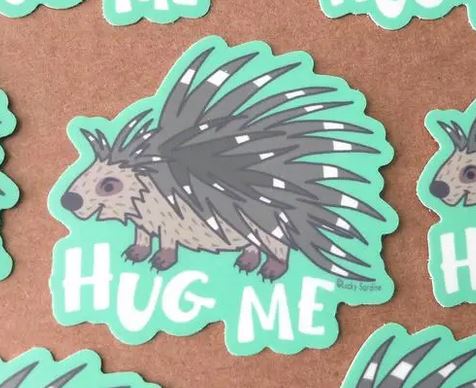 Sticker featuring a cartoon porcupine with a friendly expression and dark quills, placed on a brown background with a green outline. The vinyl sticker from Lucky Sardine includes the text "Hug Me" below and offers multiple water-resistant copies for long-lasting appeal.