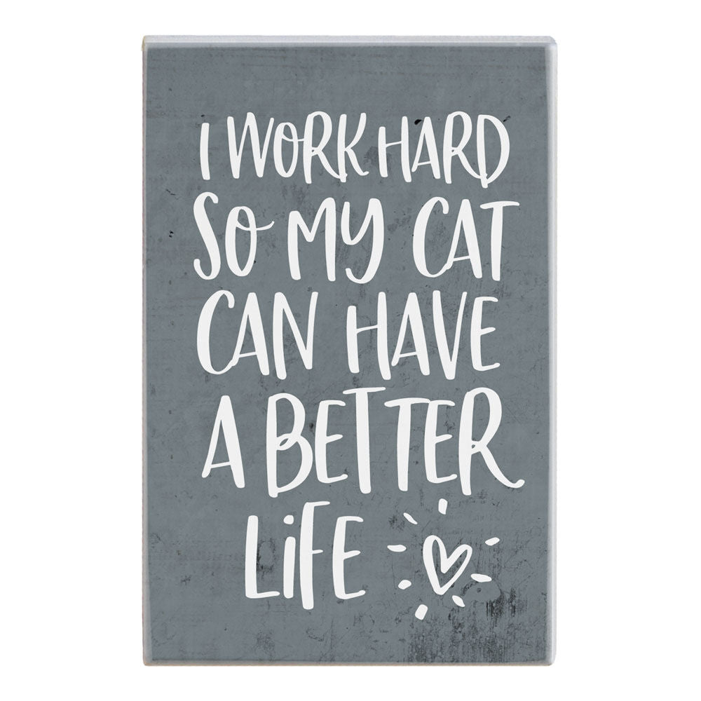 The Better Life Cat sign by SincereSurroundings is a handcrafted gray rectangular piece with white handwritten text saying, "I work hard so my cat can have a better life," embellished with a small heart and lines resembling rays of light. This charming item adds a whimsical touch to any room in your home, straight from Rock Rapids.