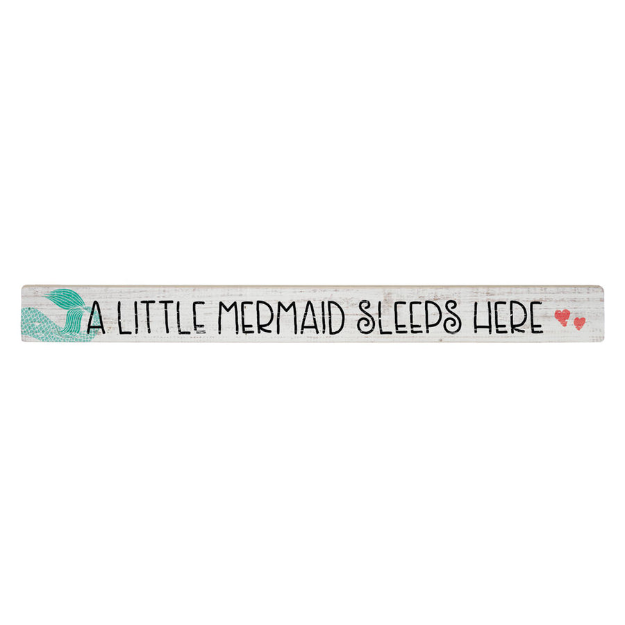 The Little Mermaid by SincereSurroundings features a handcrafted white wooden plank with the whimsical text "A LITTLE MERMAID SLEEPS HERE" printed in black font. An illustration of a mermaid tail adorns the left side, while two small, red heart illustrations decorate the right, making it perfect for displaying in your little one's room.