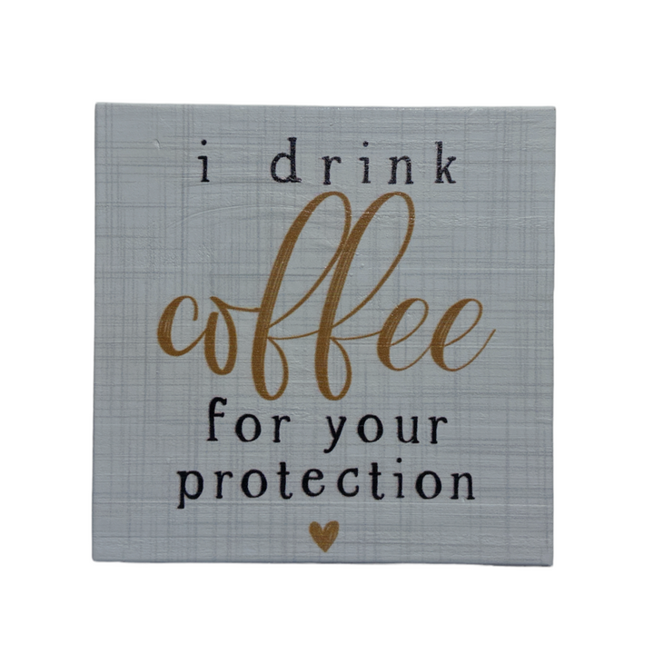 The SincereSurroundings "Coffee Protection" sign is a handcrafted grey square with a textured finish, ideal for shelf displays. It features the humorous phrase "I drink coffee for your protection" in bold black and gold letters, complemented by a charming small gold heart beneath the text.