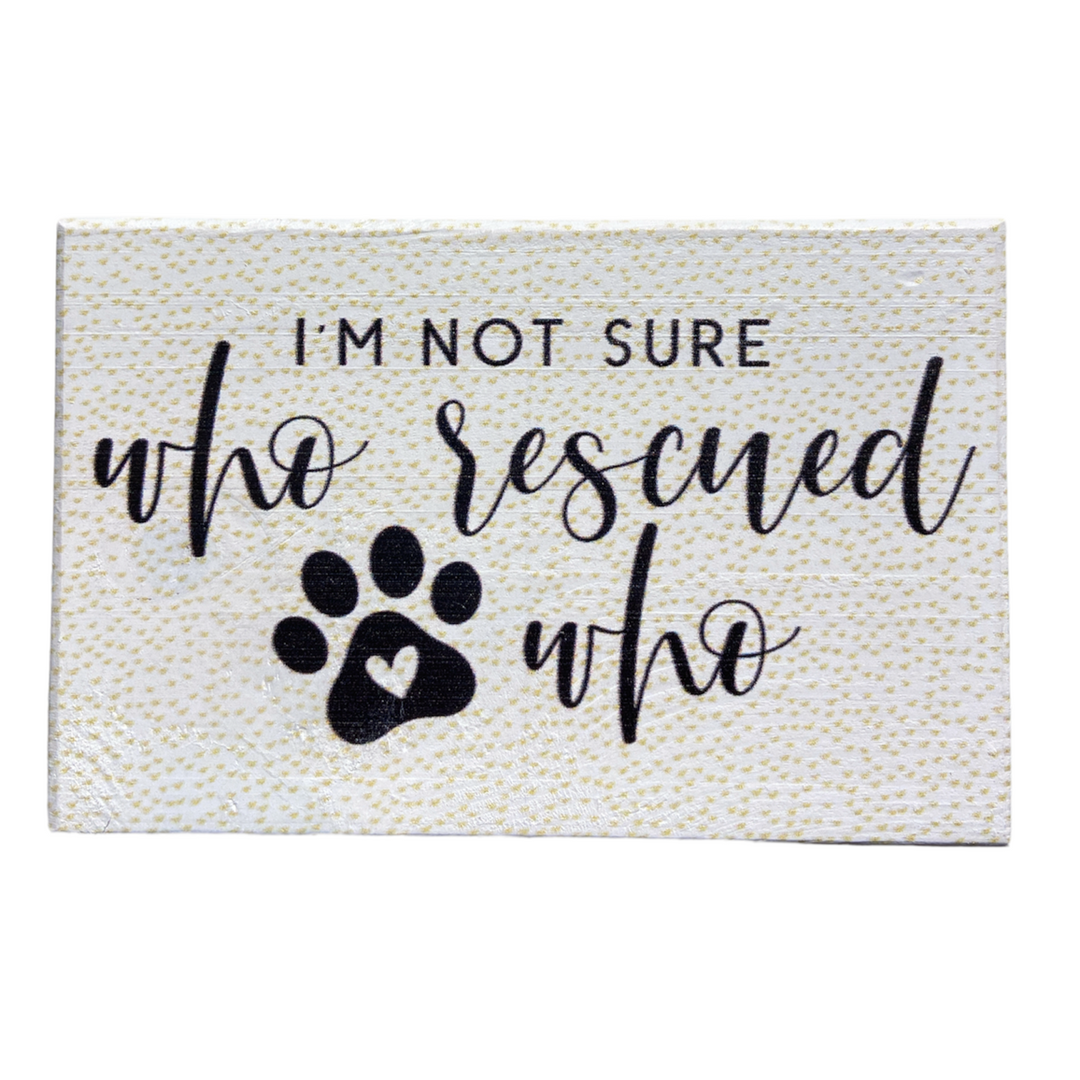 The "Who Rescued Who" decorative sign by SincereSurroundings is a beautifully handcrafted piece featuring the sentimental message, "I'm not sure who rescued who," elegantly written in cursive font. The design includes a charming paw print with a heart at its center. Easy to display, this sign boasts a white background with a subtle pattern, adding an elegant touch to any space.