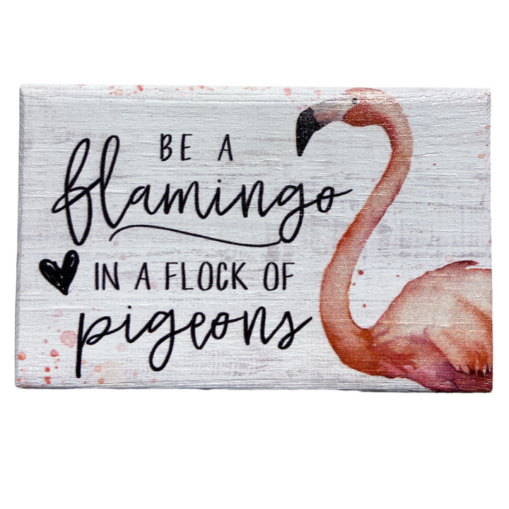 The "Be A Flamingo" sign by SincereSurroundings features a white rectangular design that's ideal for shelf displays. It boasts the phrase "Be a flamingo in a flock of pigeons" in elegant black script with a black heart, complemented by a handcrafted illustration of a flamingo on the right side, bringing charm and uniqueness to any Rock Rapids home.