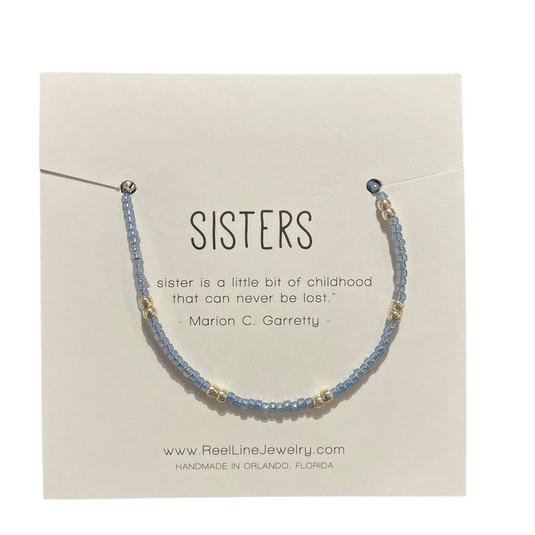 The "Sisters - Cool Blue and Silver" bracelet from Reel Line Jewelry, featuring blue and silver beads, is beautifully displayed on a card with the quote: "Sisters - sister is a little bit of childhood that can never be lost." - Marion C. Garretty. This handcrafted jewelry piece from Orlando, Florida includes adjustable links for a perfect fit.