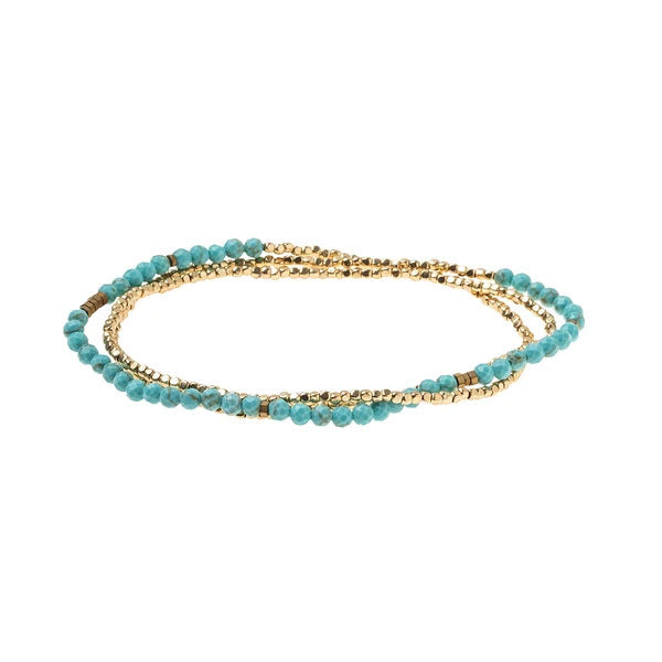 The Turquoise/Gold Delicate Wrap by Scout Jewelry highlights a captivating spiral pattern with alternating small turquoise gemstone beads and gold square beads. This minimalist piece exudes elegance, while its vibrant and metallic tones stand out brilliantly against a pristine white backdrop.