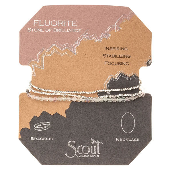 The Fluorite/Silver Delicate Wrap by Scout Jewelry includes two strands of iridescent fluorite crafted from semi-precious gemstone beads. The packaging emphasizes the stone's qualities: inspiring, stabilizing, and focusing. Labels indicate that it can be worn both as a versatile bracelet and necklace.