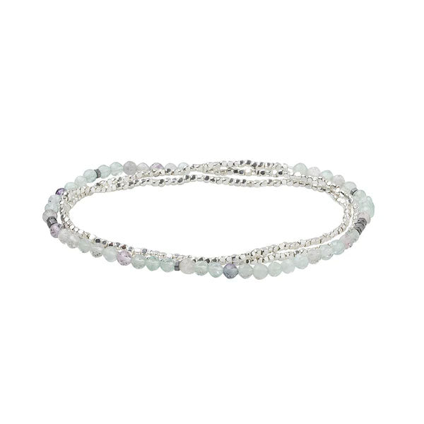 The Fluorite/Silver Delicate Wrap by Scout Jewelry is an elegant piece, showcasing a multi-strand design adorned with small, round fluorite and silver beads in light blue tones. This bracelet necklace is artfully arranged in a circular shape on a plain white background.