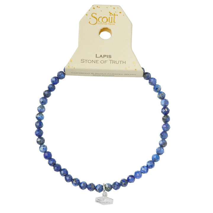 A Mini Bracelet Lapis/Silver from Scout Jewelry, crafted with deep blue, semi-precious faceted lapis stone beads, is displayed against a white background. The bracelet features a small silver charm hanging from it. The packaging prominently reads "Scout" at the top and "Lapis, Stone of Truth" below.