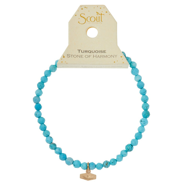 Introducing the Mini Bracelet Turquoise/Gold by Scout Jewelry: a stunning turquoise beaded bracelet featuring faceted stone beads and a small gold charm with a hand symbol. This elegant piece is displayed on a beige card that reads "Scout" at the top and "Turquoise Stone of Harmony" below. Crafted with semi-precious gemstones and strung on a durable stretch cord, it’s both beautiful and resilient.