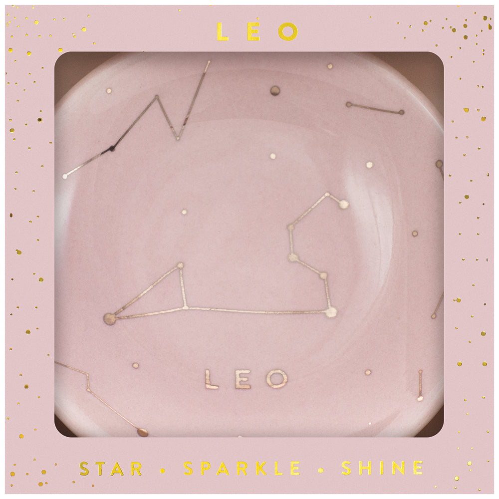 In a square, star-studded pink box, LuckyFeather's Dish Leo features a decorative Zodiac Trinket Dish with the Leo constellation design. The constellation is illustrated with gold dots and lines, while the text "LEO" appears below it on the plate. The box is labeled "LEO" at the top and "STAR SPARKLE SHINE" at the bottom.