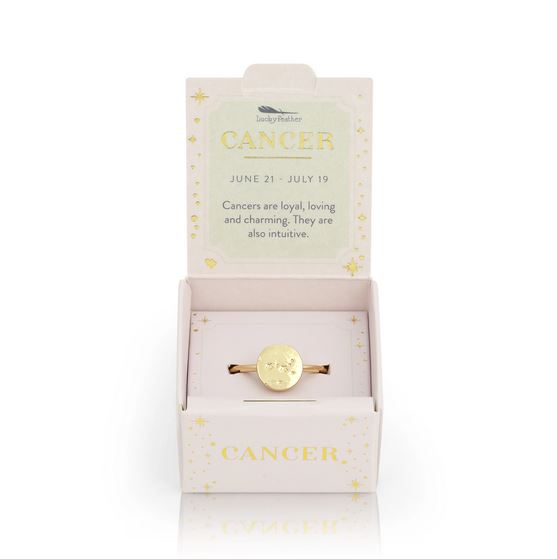 A stunning Cancer Signet Ring from LuckyFeather, dipped in 14k gold and featuring the Cancer zodiac symbol, is beautifully showcased in an open box. The lid states, "CANCER, June 21 - July 19. Cancers are loyal, loving, and charming. They are also intuitive." The ring's adjustable band enhances the versatility of its starry, celestial-themed packaging.