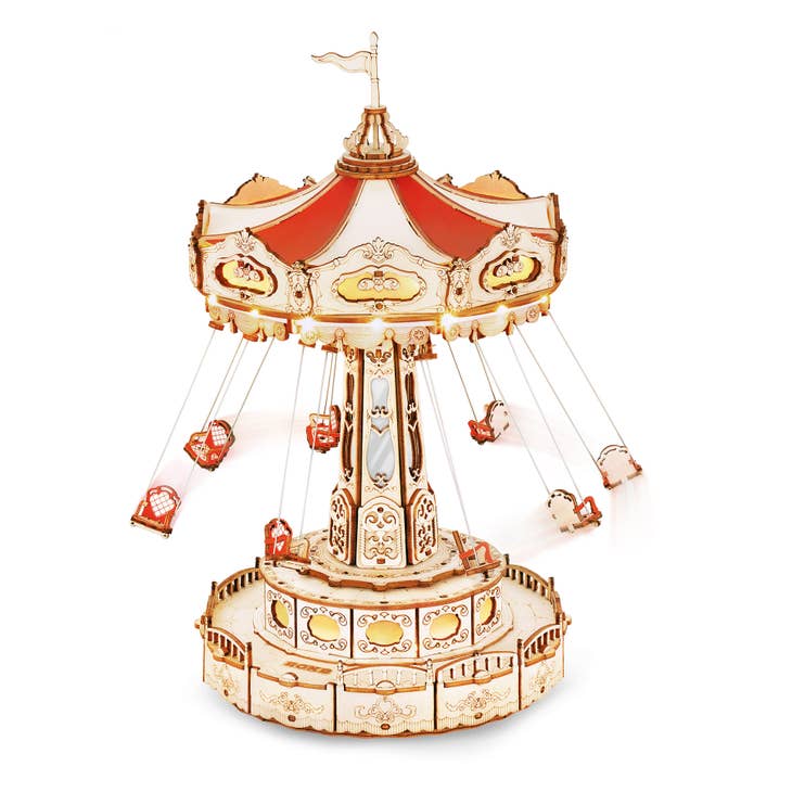 The Electro-Mechanical Wooden Puzzle: Swing Ride by Hands Craft is a model with intricate, detailed designs and is part of the amusement park series. This swing ride features seven open swings hanging from a canopy decorated with red and white panels, crowned by a flag. Its base includes a fenced platform adorned with ornate patterns.