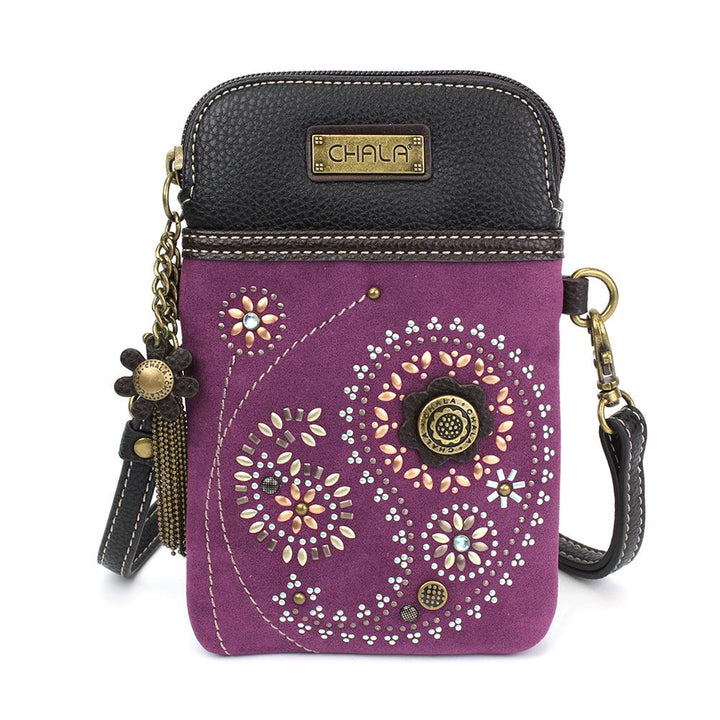 Introducing the Dazzled Cell Xbody - Paisley by Chala: a compact crossbody bag featuring a black leather top and a purple fabric body. Decorated with an array of floral and swirl patterns in vibrant colors, it comes complete with a metal brand plate, a flower-shaped charm, and an adjustable, detachable strap.