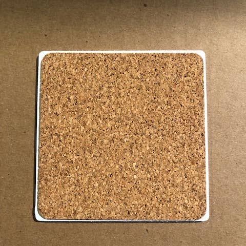 A Diddley Squats Routine coaster from Drinks On Me rests on a brown surface, its simple design accentuating the natural texture of cork. In contrast to resin coasters, this one embraces simplicity and warmth.