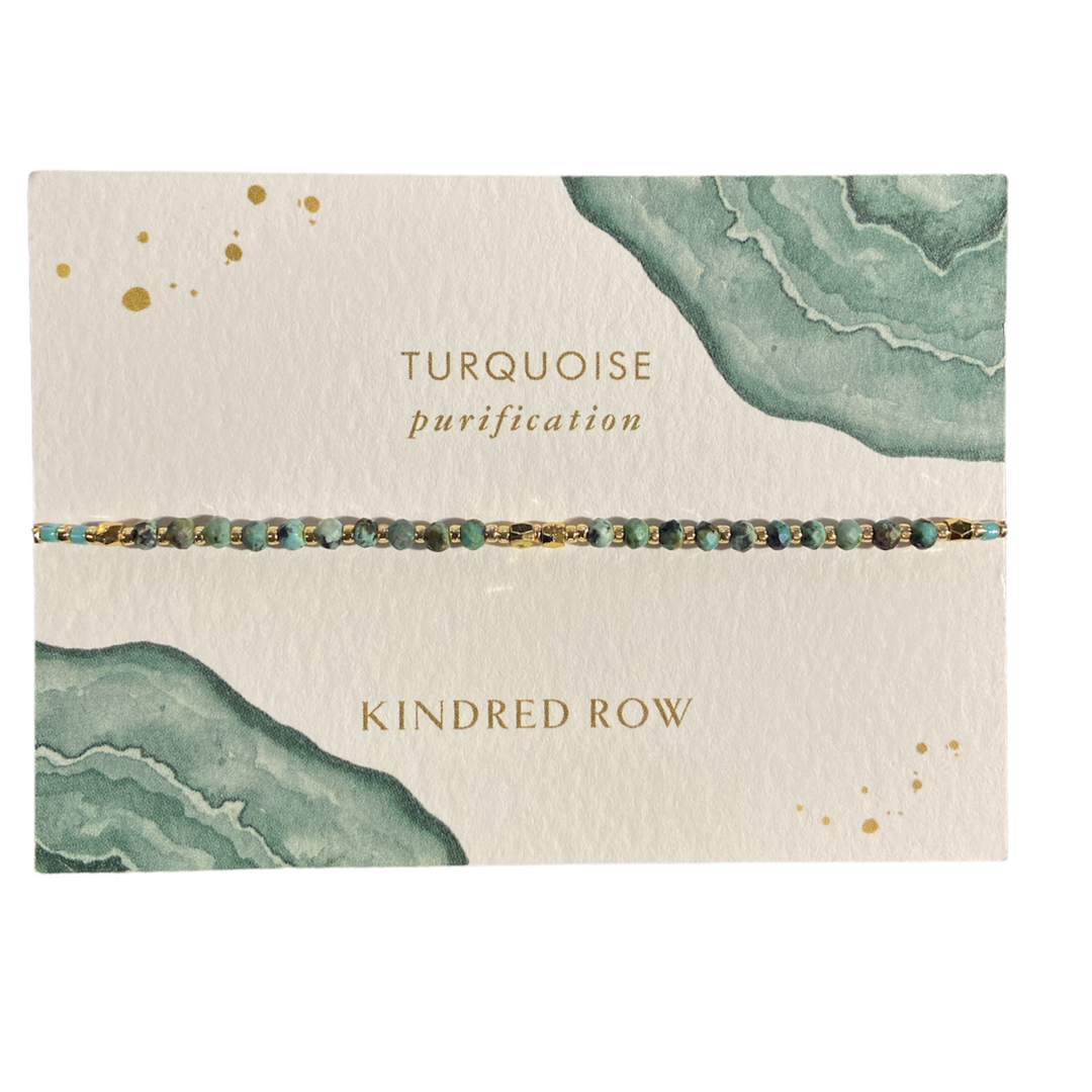 A delicate handmade "Turquoise Healing Gemstone Stacking Bracelet" from Kindred Row is displayed on a white card with a watercolor design in green hues. The card reads "Turquoise purification" and showcases this elegant piece featuring natural turquoise and gold accents.