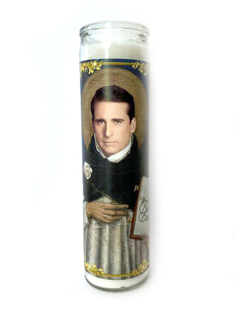 The Michael Scott Candle by BOBBYK BOUTIQUE is a tall, unscented glass candle featuring an image of a man dressed in religious attire, akin to a saint holding a book. The candle, which evokes the feel of a celebrity shrine, is decorated with gold accents and depicts him in a reverent pose.