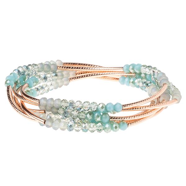 The Wrap Neptune/Rose Gold bracelet by Scout Jewelry features multiple strands adorned with small, round crystal beads in shades of blue, turquoise, and clear. These beads are elegantly arranged along thin rose gold-toned wires, creating a layered design that complements etched metal accents beautifully.