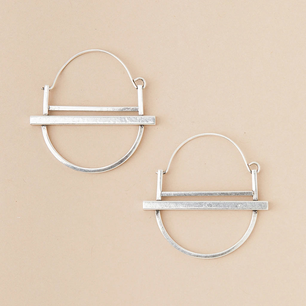 The Saturn Hoop Silver earrings by Scout Jewelry are showcased on a beige background. Each hypoallergenic earring features an open circular design intersected by a horizontal bar at the bottom, with a lightweight semi-circle below it, highlighting a minimalist and modern aesthetic.